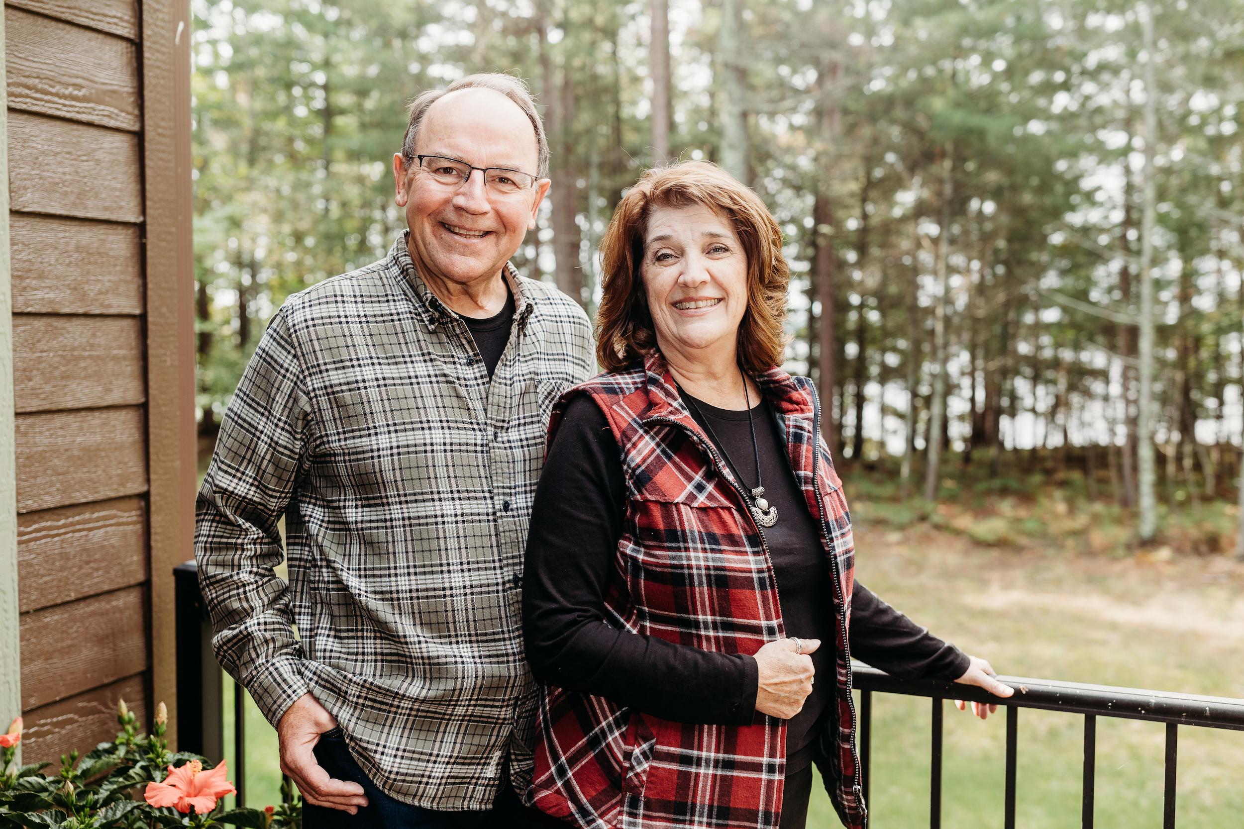 Tom and Chris Tiffany smiling on a deck with a forest background.