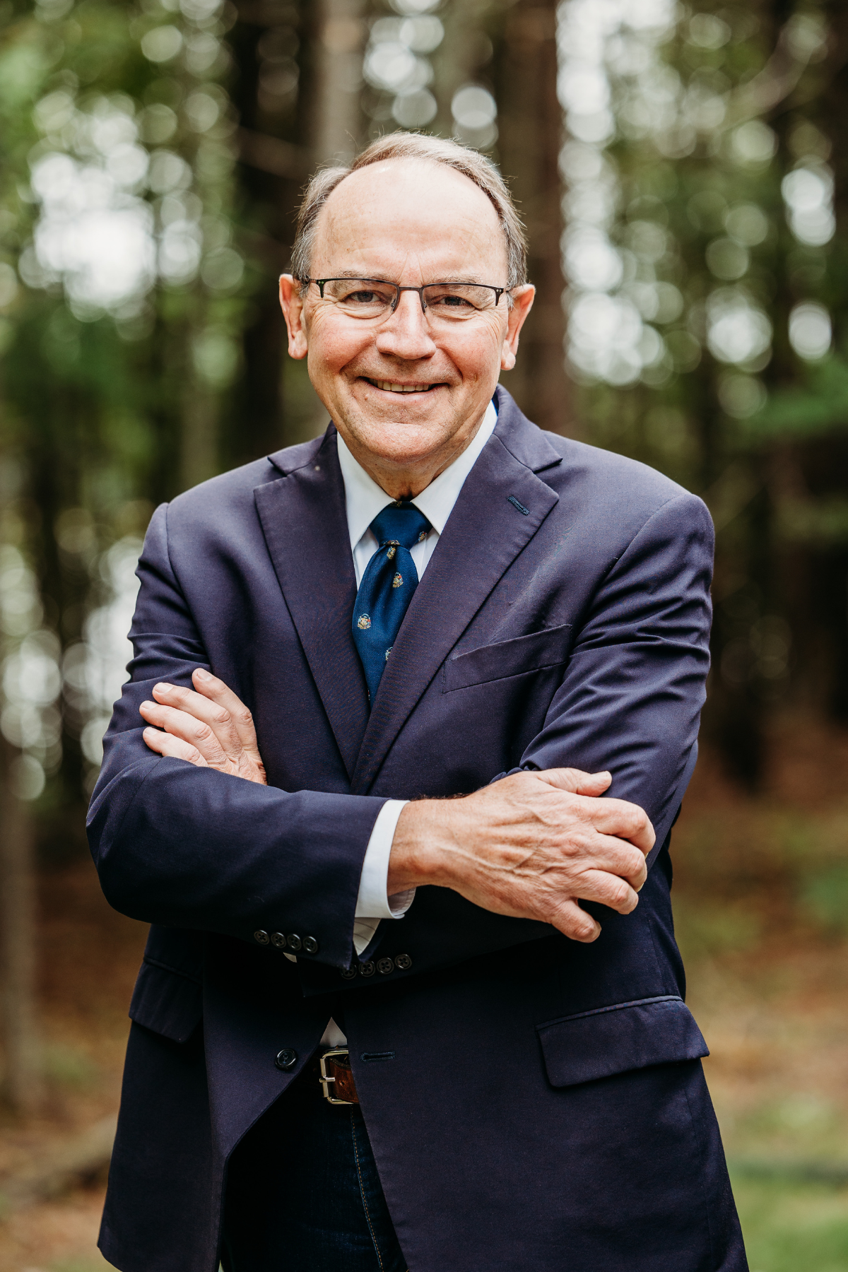 Tom Tiffany standing before a wooded background, professional.